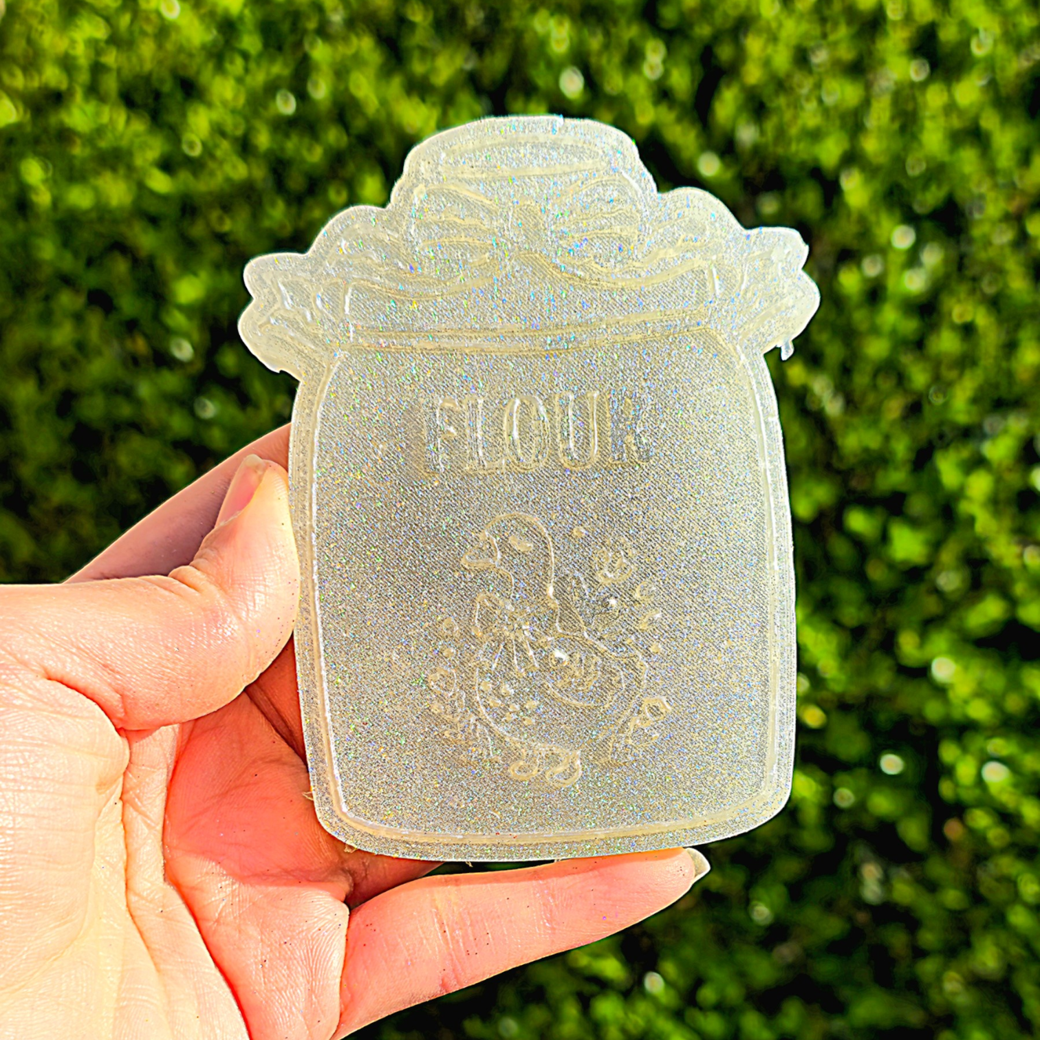 Hand holding a decorative flour jar against a green outdoor background