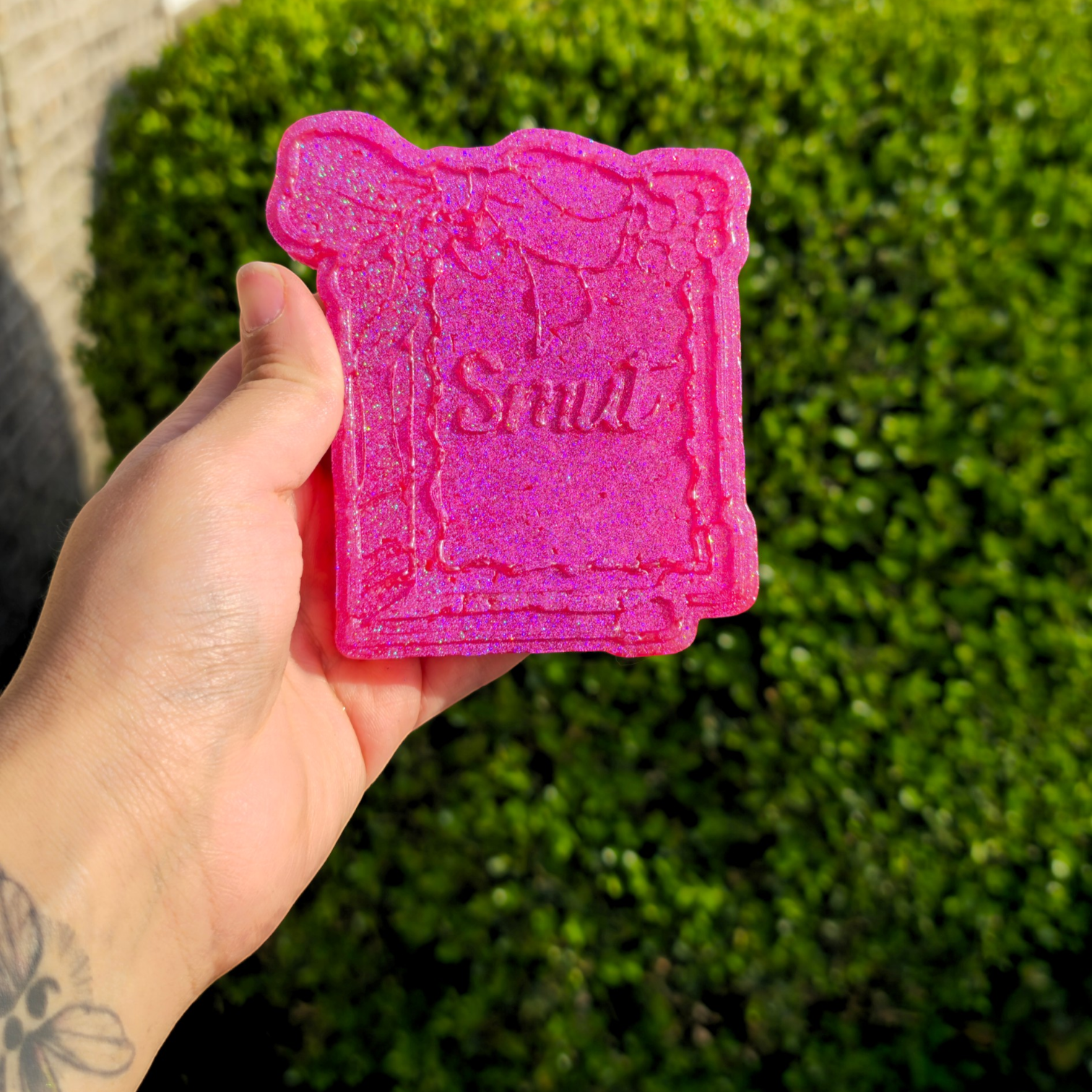 Pink 'Smile' candy mold held by a hand with a green outdoor background